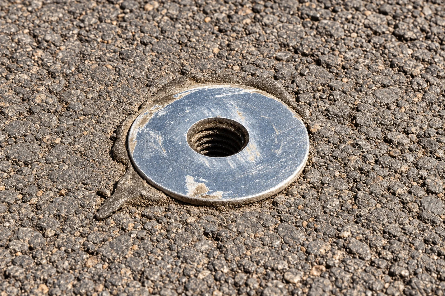 Installed silver asphalt anchor with visible internal threads, a flat flange, and an irregular bead of adhesive around the head
